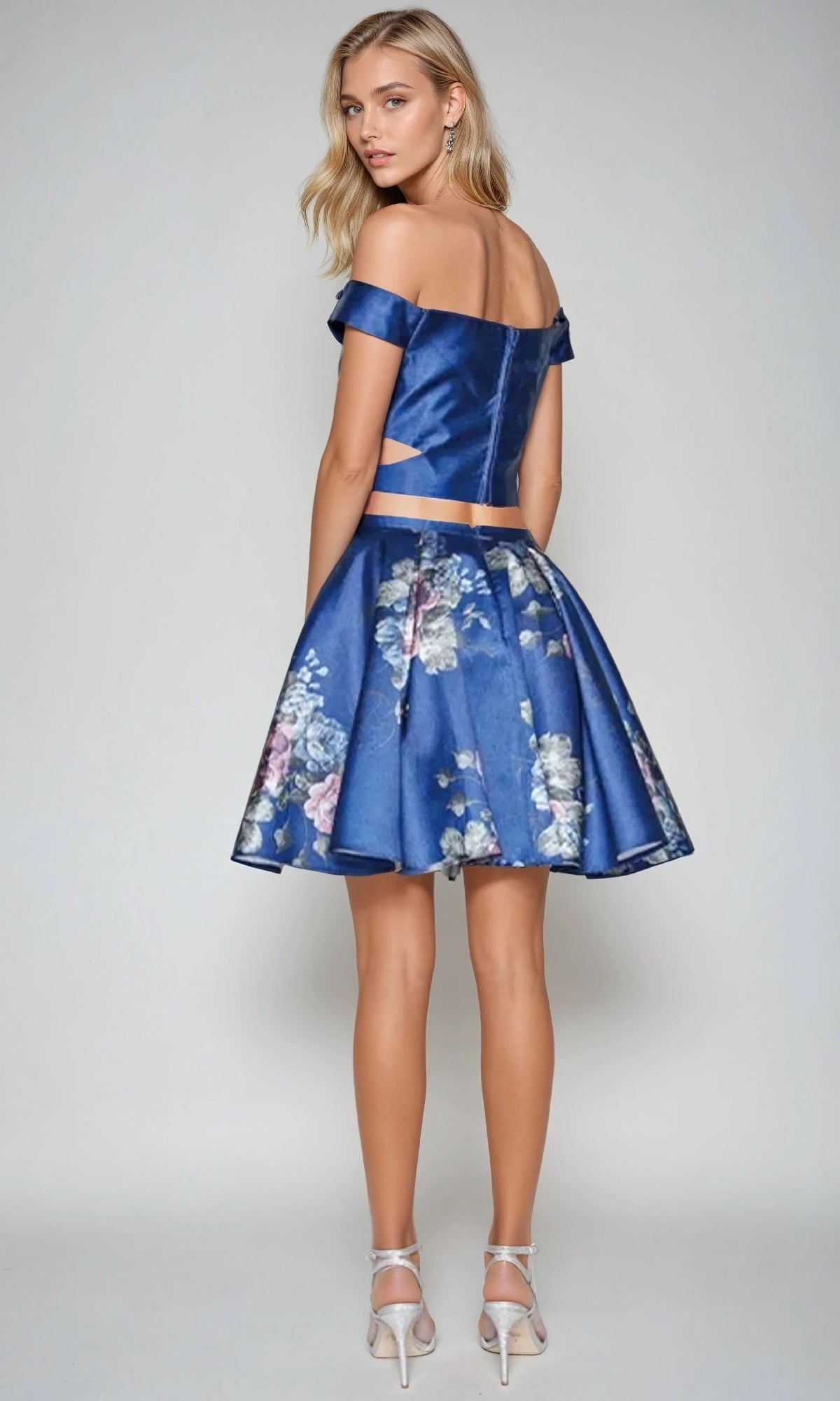 Woman in the Short Party Dress: Juliet 798 stands with her back to the camera, wearing a blue off-the-shoulder top and matching floral A-line skirt paired with white high-heeled sandals.